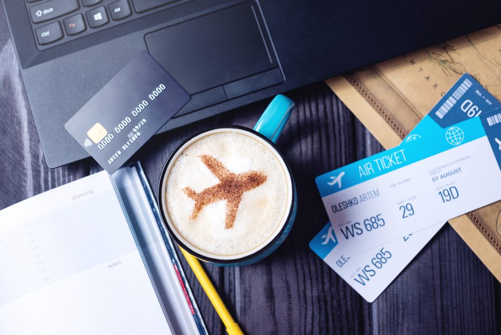 Laptop, plane tickets, coffee, cappuccino and credit card lies on the table. The view from the top. The concept of travel and transport