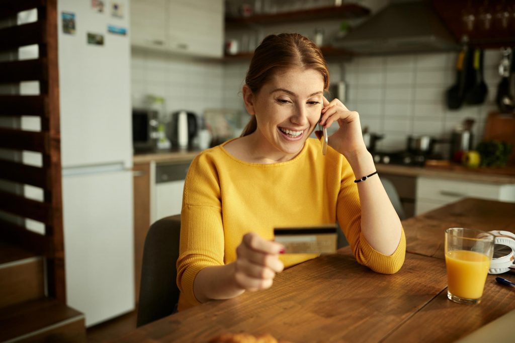 happy woman yellow shirt holding credit card talking on the phone