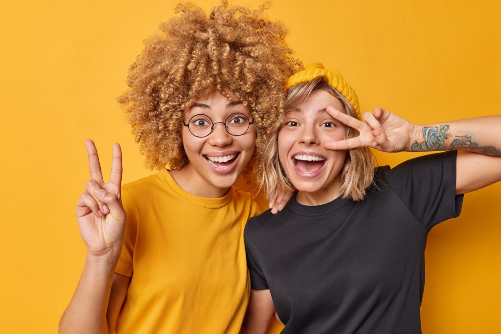two friends show peace gesture and smile holding and laughing