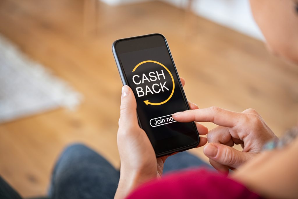 Woman taking benefit of cashback using smart phone, shopping and money refund concept. Woman hand holding smartphone with button to get started the cashback. Close up of girl holding mobile phone while clicking on join now option in app.