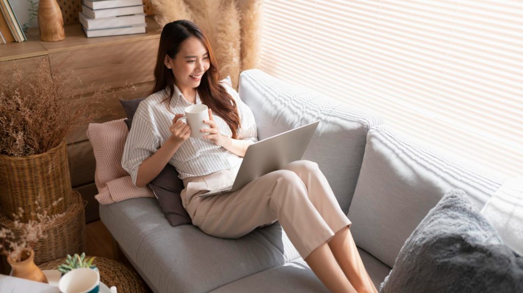young woman in the couch using laptop notebook drinking coffee tea