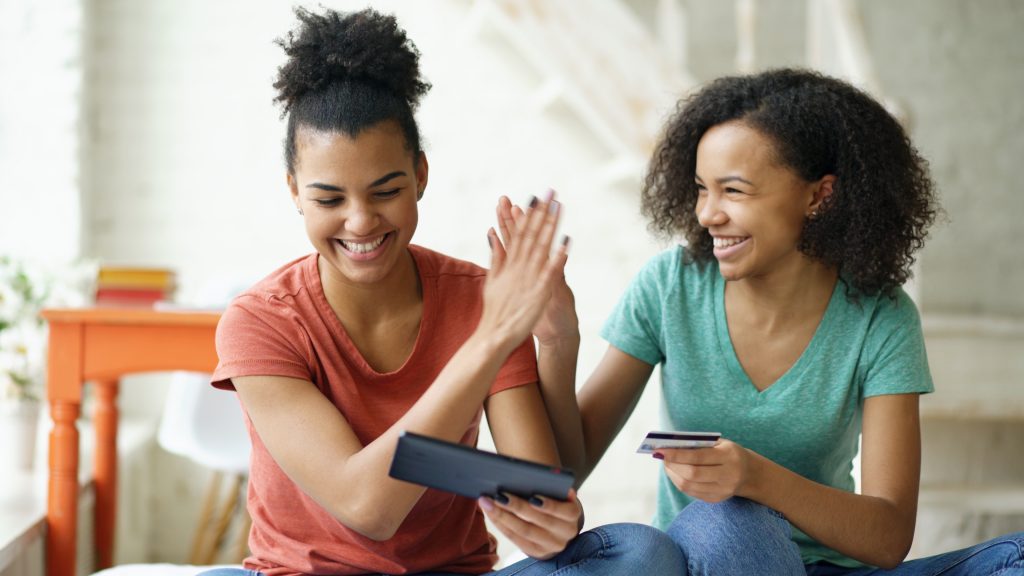 Two cheerful mixed race curly girlfriends shopping online with tablet computer and credit card