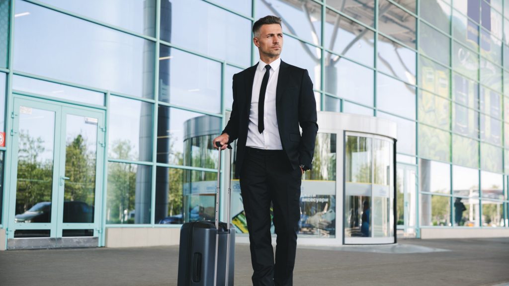 Confident mature businessman standing outside the airport with a suitcase