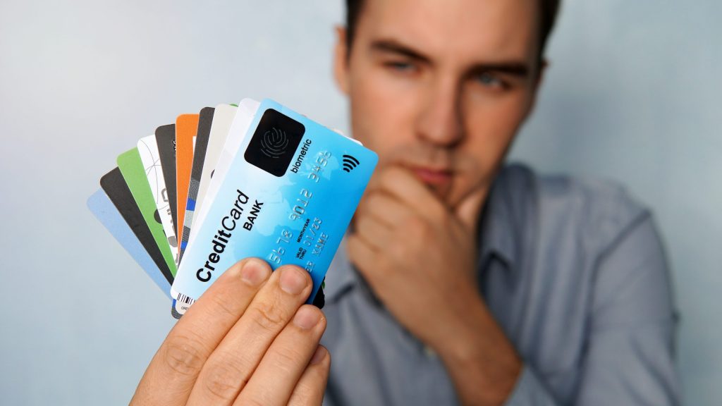 The young man is holding a stop of credit and debit cards in a pensive pose. The guy chooses a card to pay. businessman holds a large stack of credit cards in his hand and looks at them.