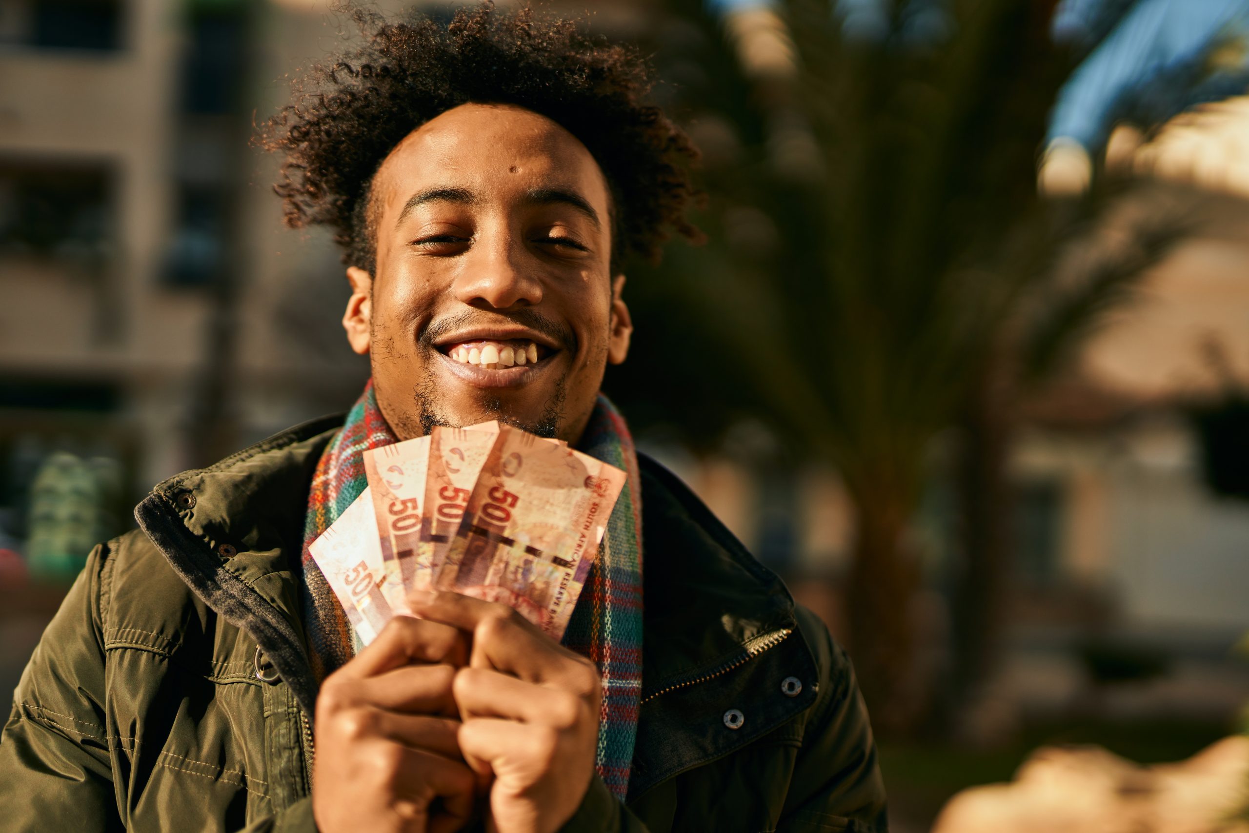 Young african american man smiling happy holding south africa rands banknotes at the city