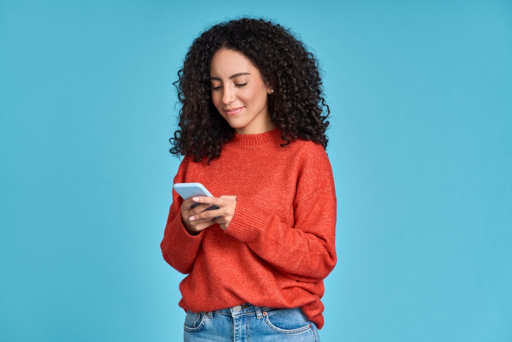 Young happy latin woman using mobile phone isolated on blue background.