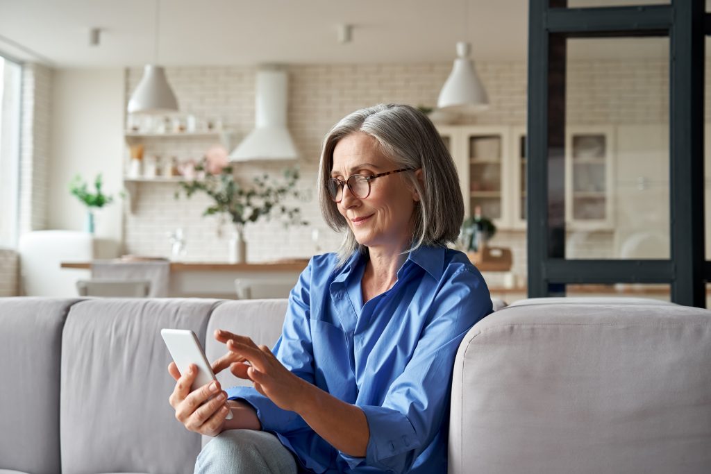 Mature old senior woman using smartphone sitting on sofa at home.